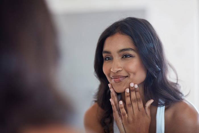 beautiful woman touches her face while looking in the mirror